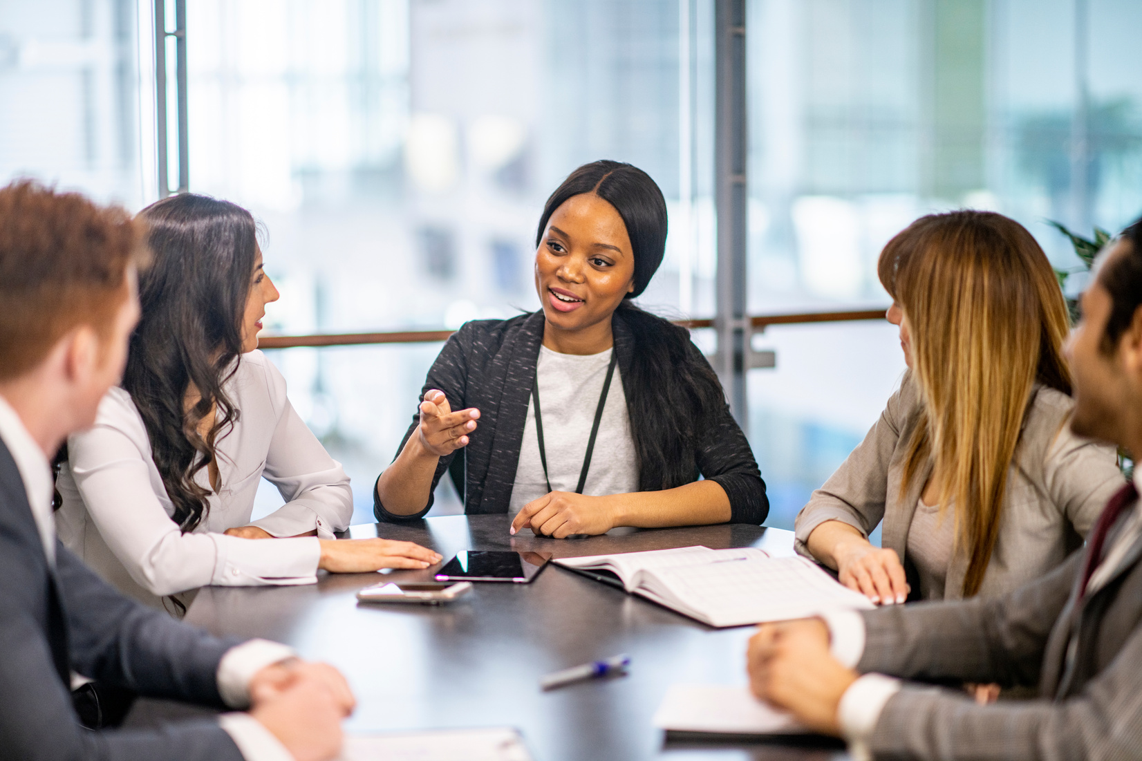 A confident female-presenting executive is addressing four colleagues at a boardroom table.