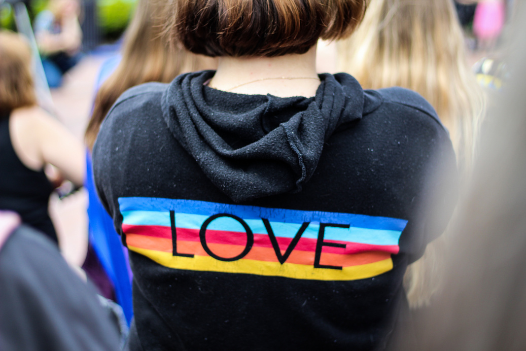 A person is wearing a black hoodie with the pride flag across the back and the word LOVE.